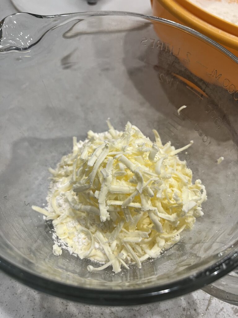 Self rising flour in a glass bowl with grated butter in it.