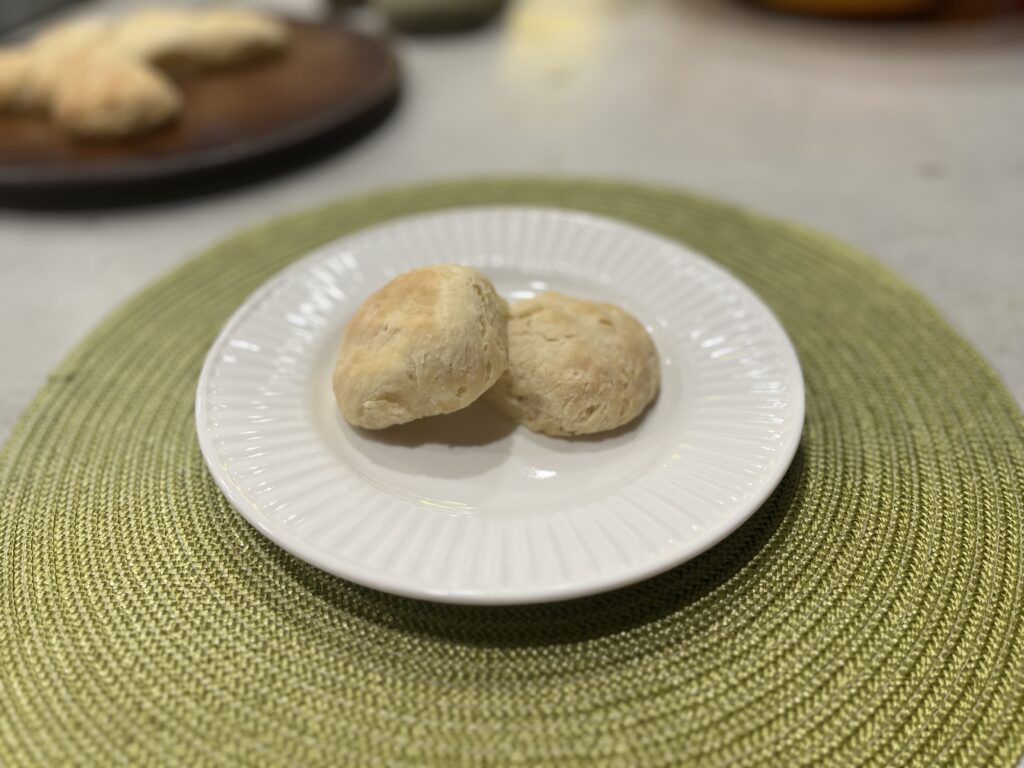 Two homemade biscuits on a white plate sitting on a green placemat.