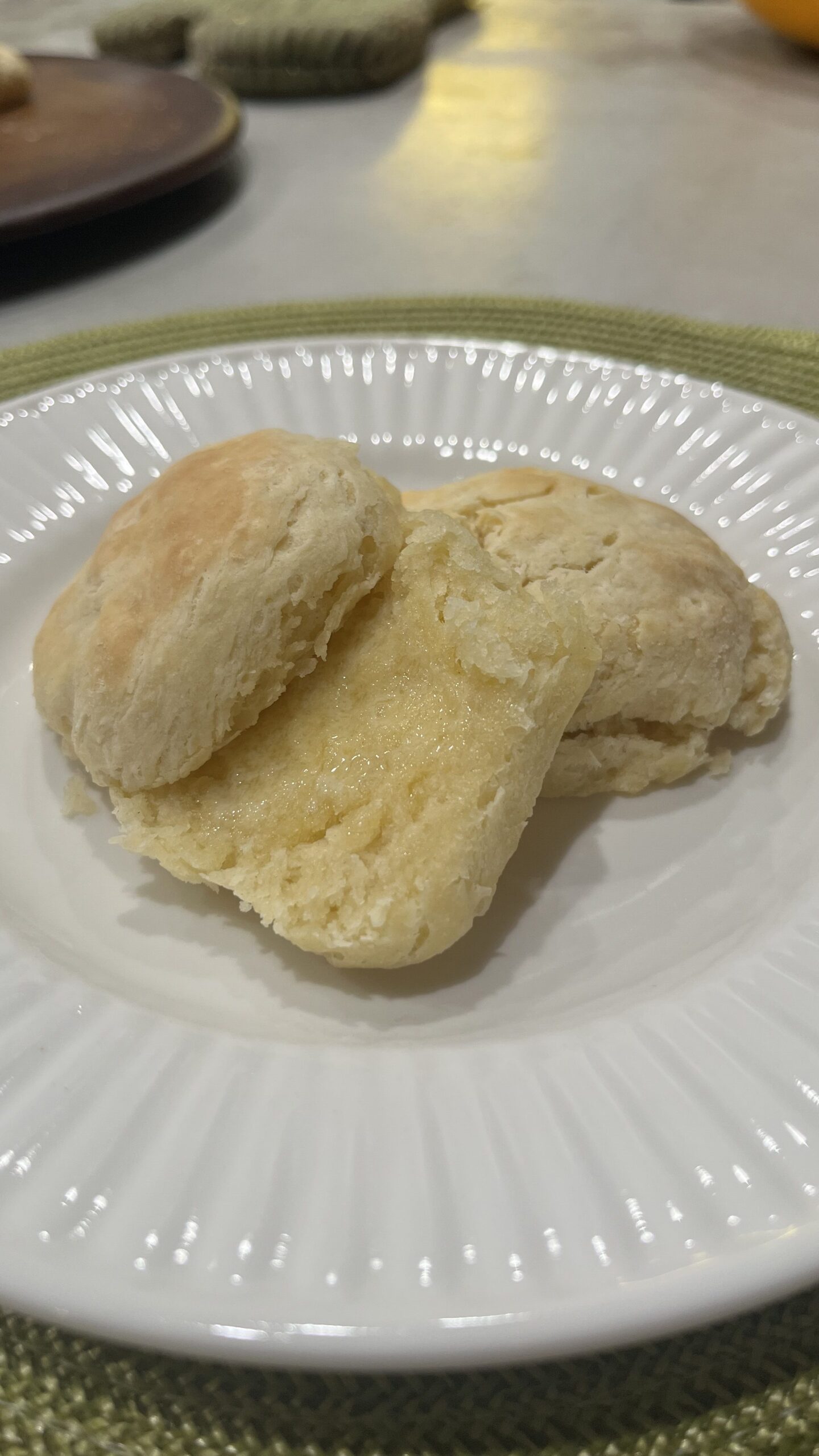 Homemade biscuits on a white plate. One is cut open with melted butter inside.